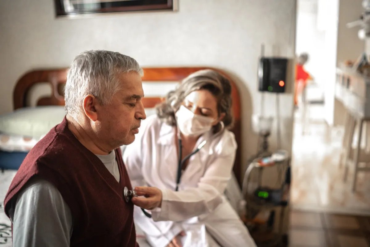 A health visitor uses a digital tablet and talks to an elderly man during his visit